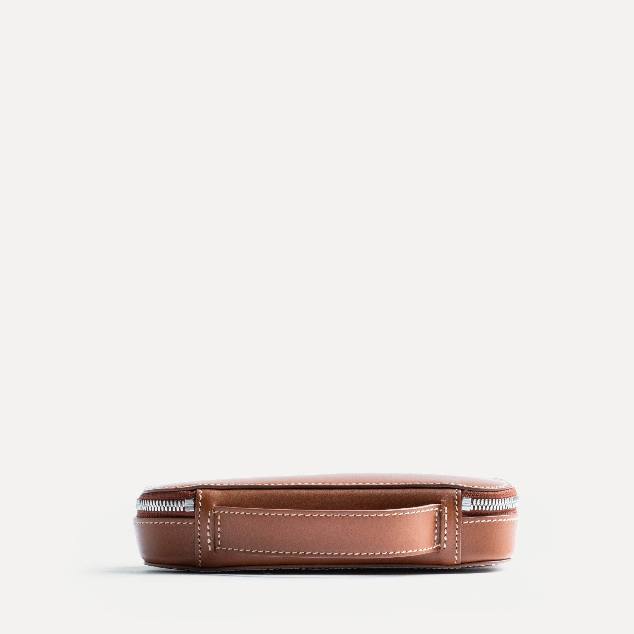 Trousse de toilette homme en cuir cognac avec une poignée arrière intégrée.