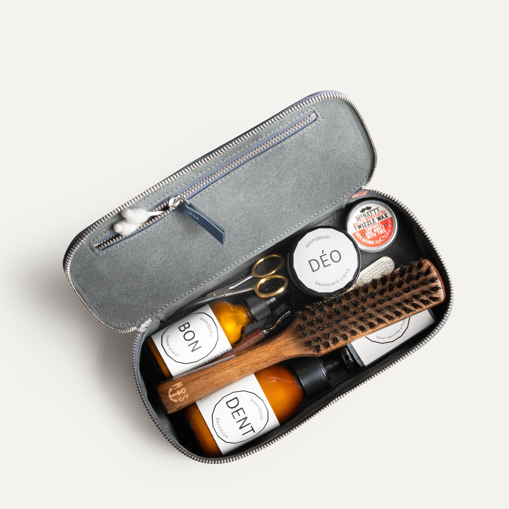 Trousse de toilette homme luxe remplie de produits de soin, vue intérieure avec accessoires rangés.
