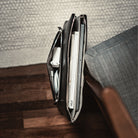 Pochette Mac ANNA en cuir noir vue du dessus, posée au sol, remplie de magazines, chargeur et ordinateur.