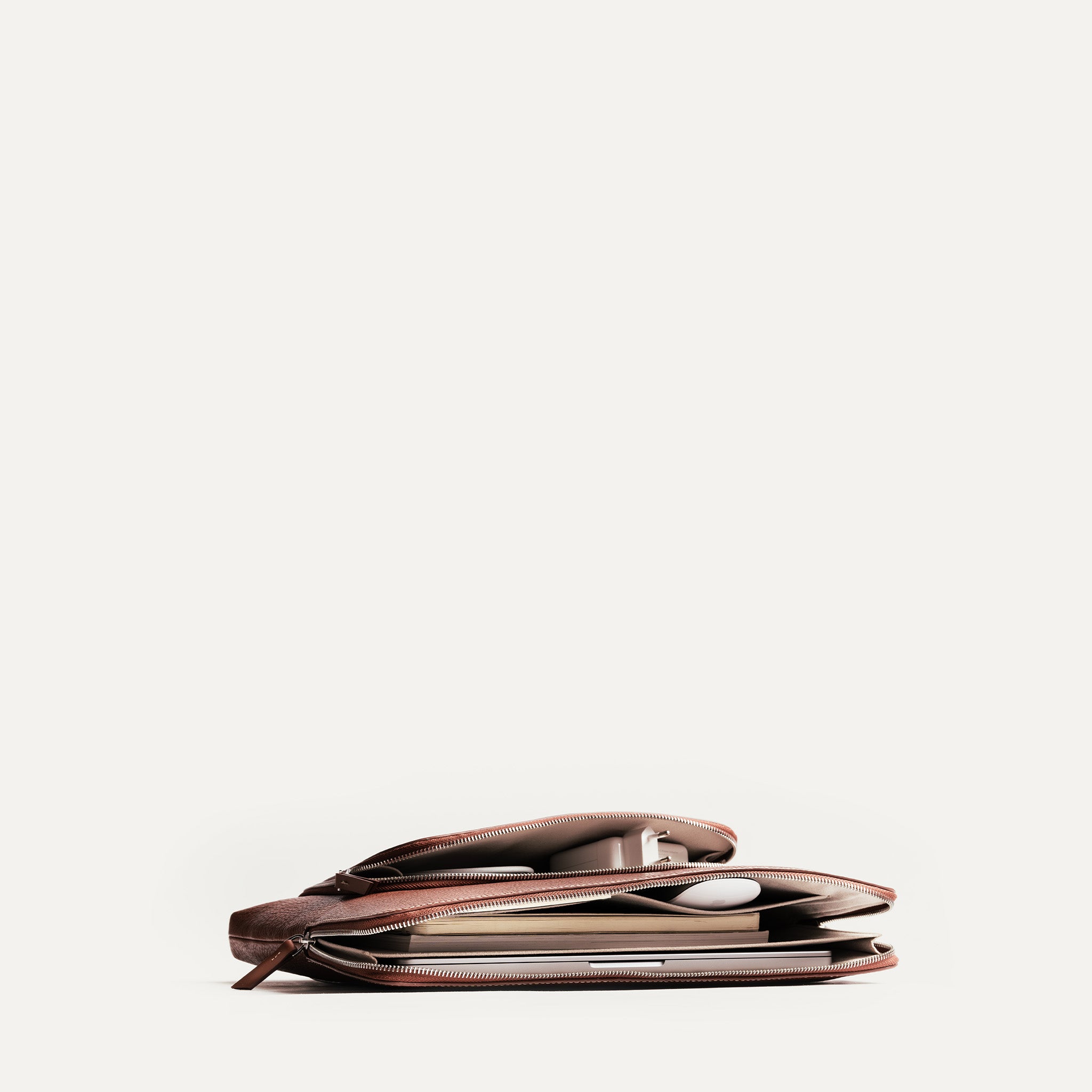 Vue lifestyle de la pochette ordinateur cuir ANNA remplie de documents, chargeur et ordinateur portable.