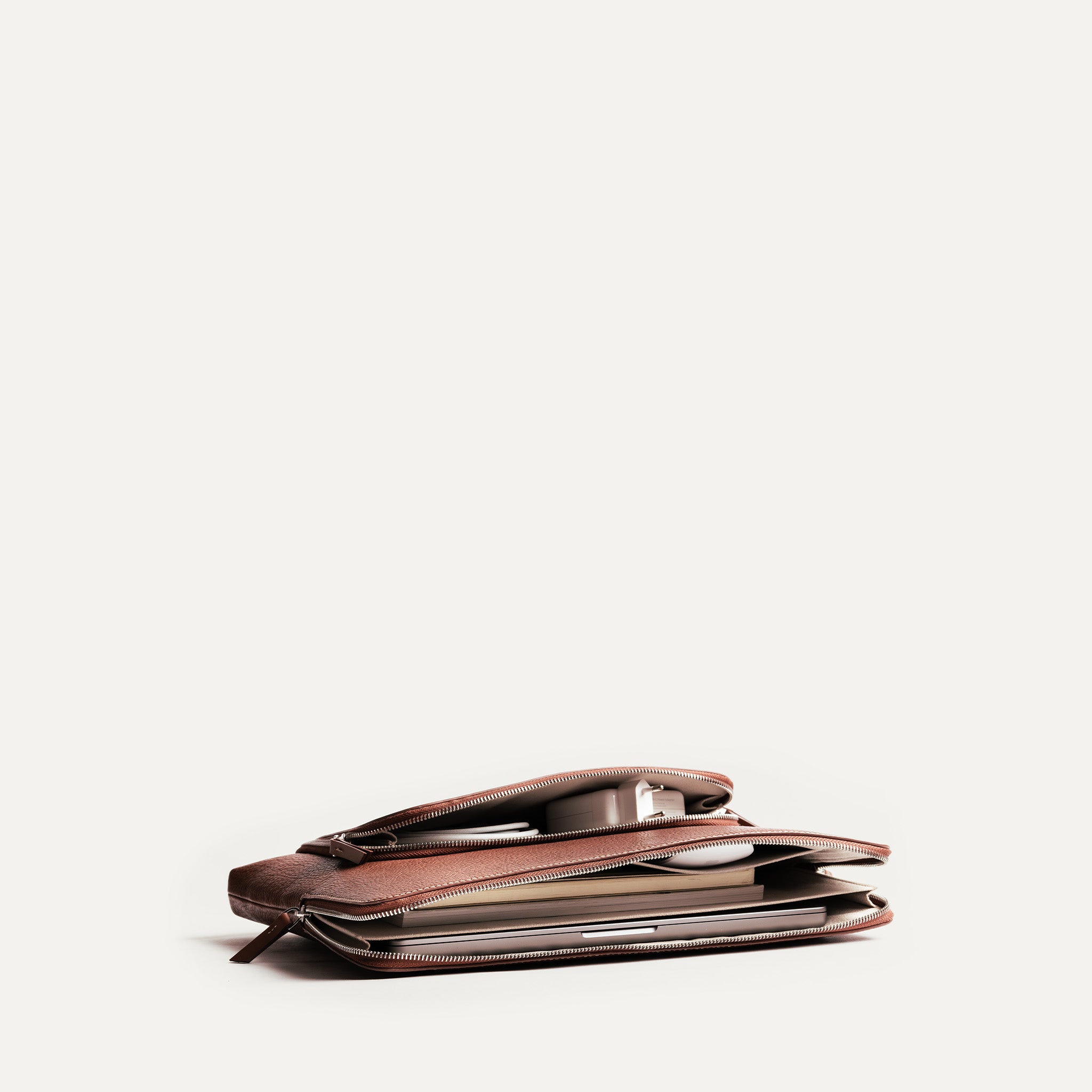 Pochette ordinateur femme en cuir, compartiment principal et poches ouvertes pour chargeur et câbles.
