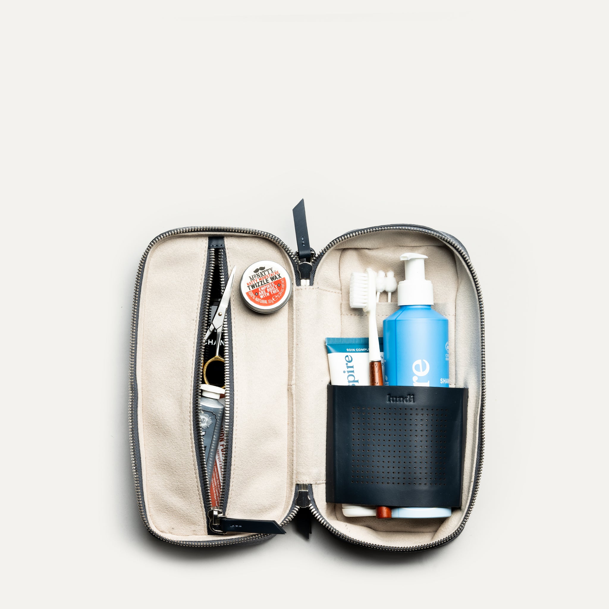 Trousse de toilette cuir pour homme ouverte avec produits de soin et compartiments de rangement astucieux.