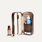 Trousse de toilette femme marron ouverte en partie, illustrant les compartiments internes et les produits de soin.