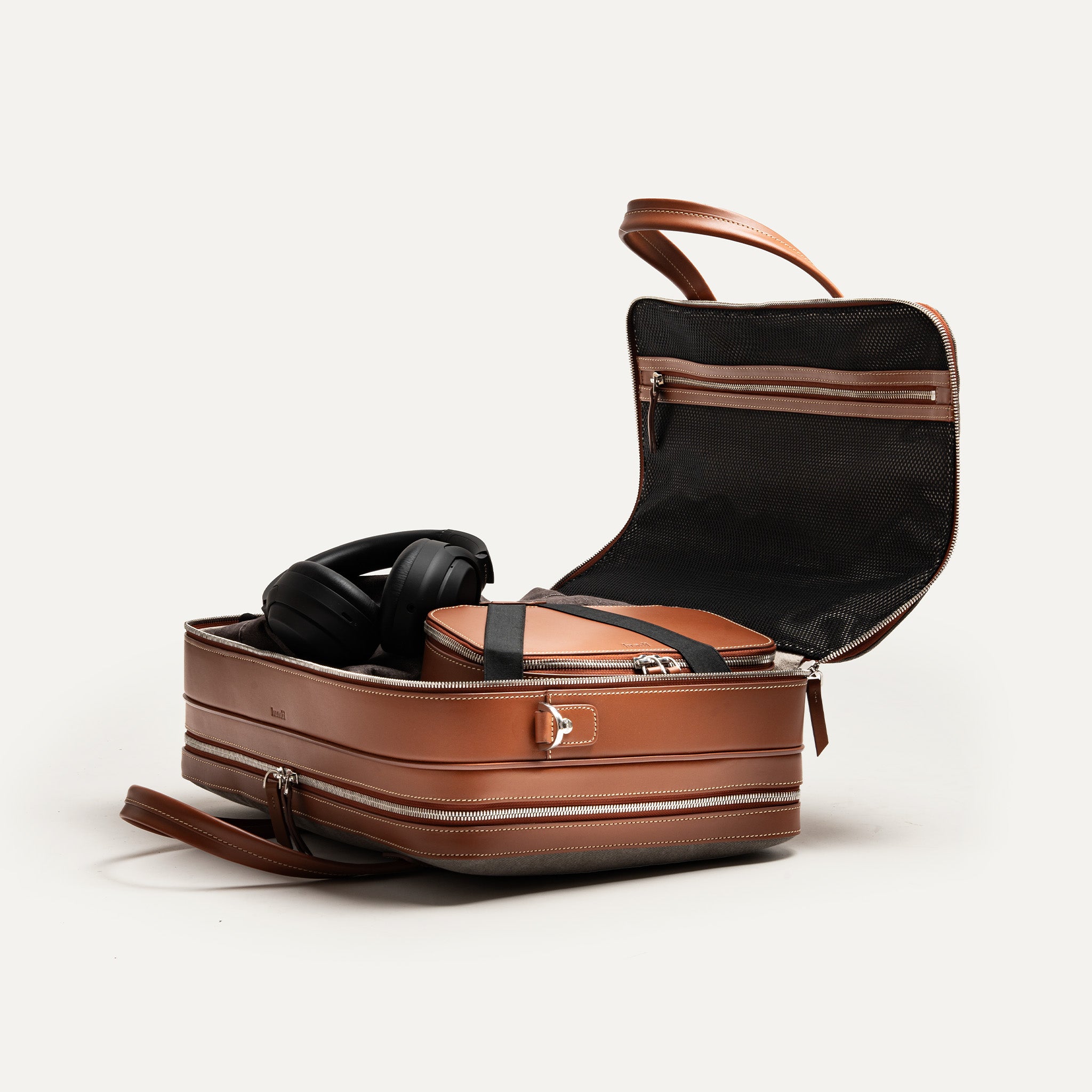 Cartable cuir cognac et toile grise avec compartiment dressing équipé d’une sangle élastiquée pour maintenir les vêtements.