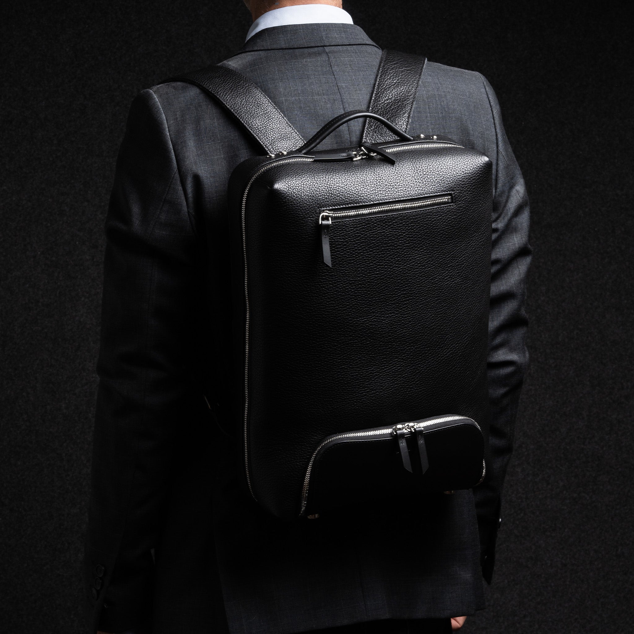sac à dos homme en cuir porté avec un costume, idéal pour un style business chic.