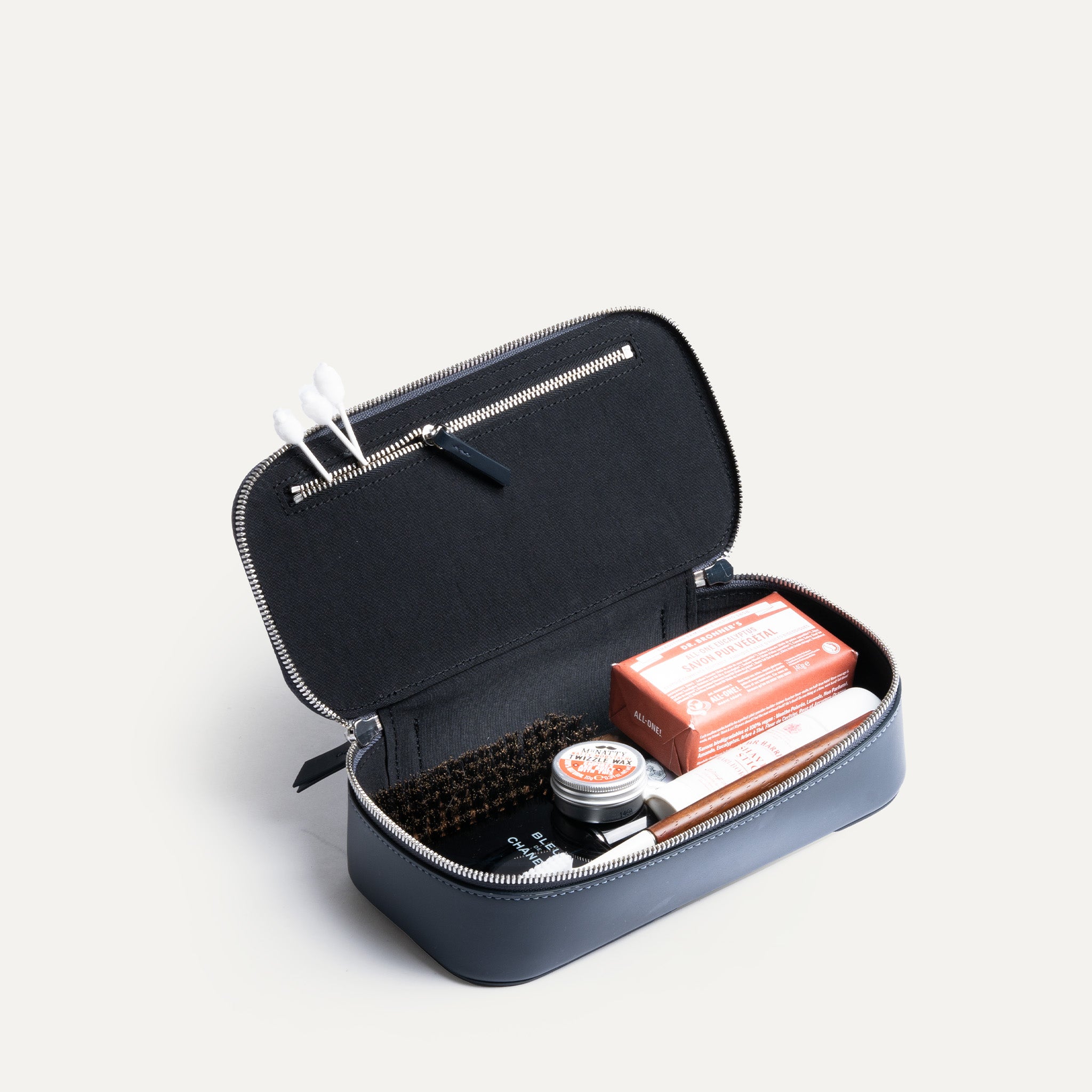 Grande trousse de toilette pour homme ouverte, montrant des produits de soin et une poche intérieure zippée.