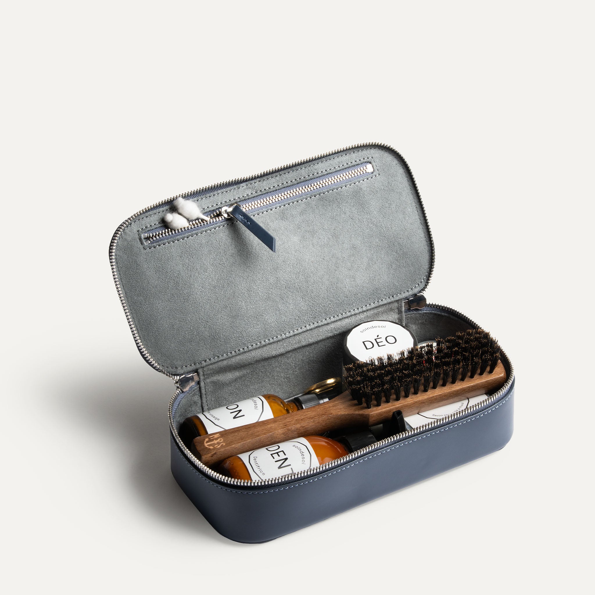 Grande trousse de toilette pour homme ouverte, montrant des produits de soin et une poche intérieure zippée.