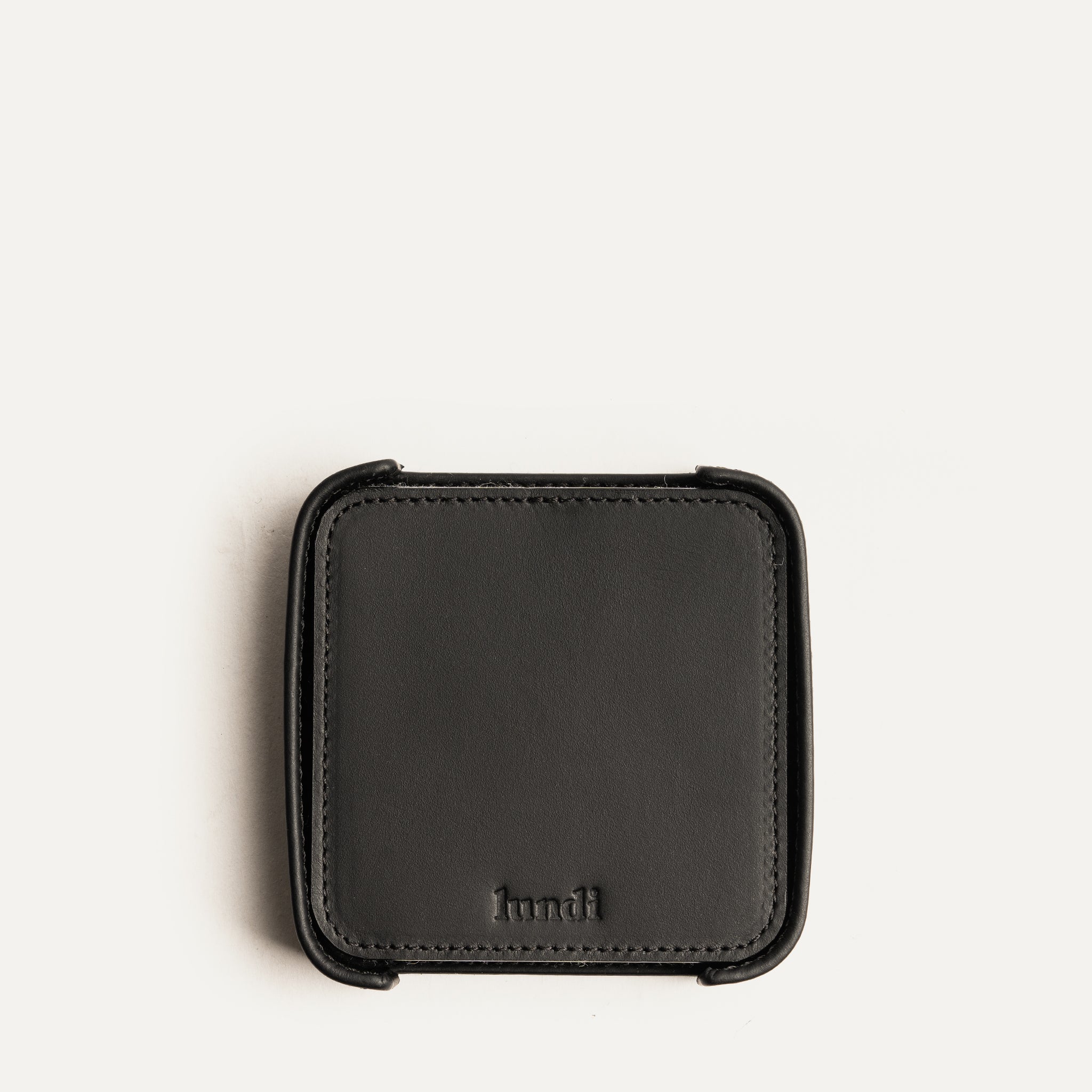 Dessous de verre en cuir noir vide vu du dessus, avec logo embossé lundi, fond clair épuré.