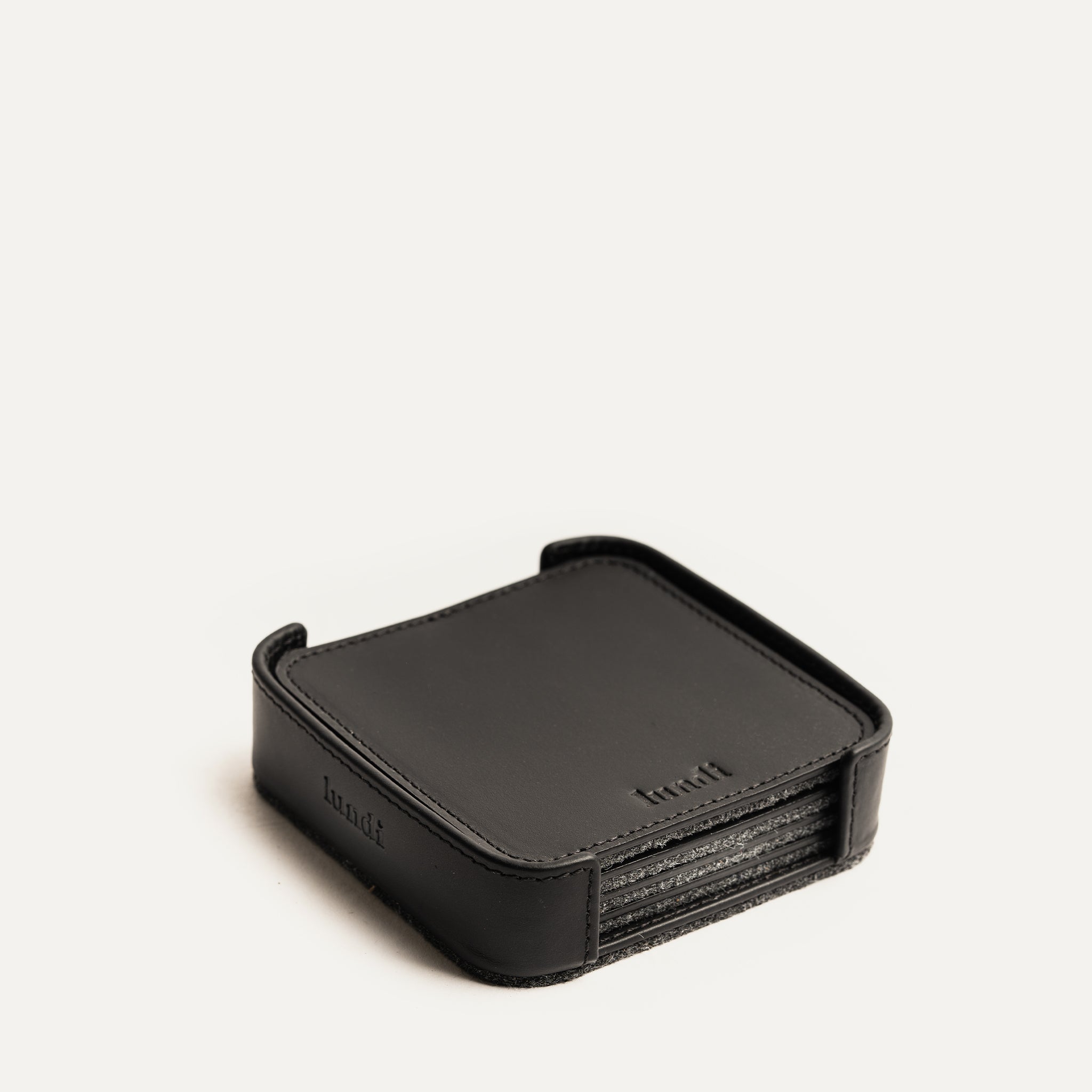 Dessous de verre en cuir noir dans un support assorti, empilé de façon ordonnée sur fond blanc.