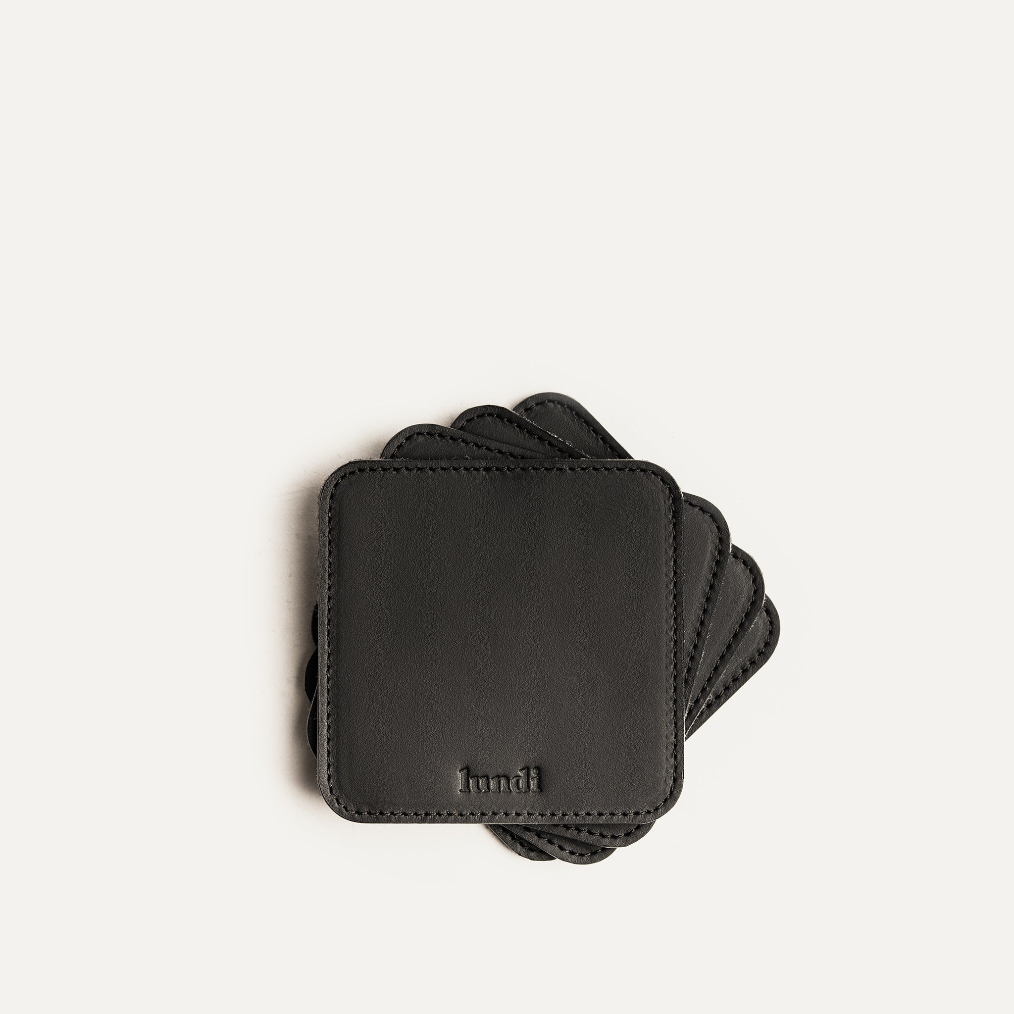 Dessous de verre noir en cuir, éparpillés en éventail avec logo embossé lundi visible sur le dessus.