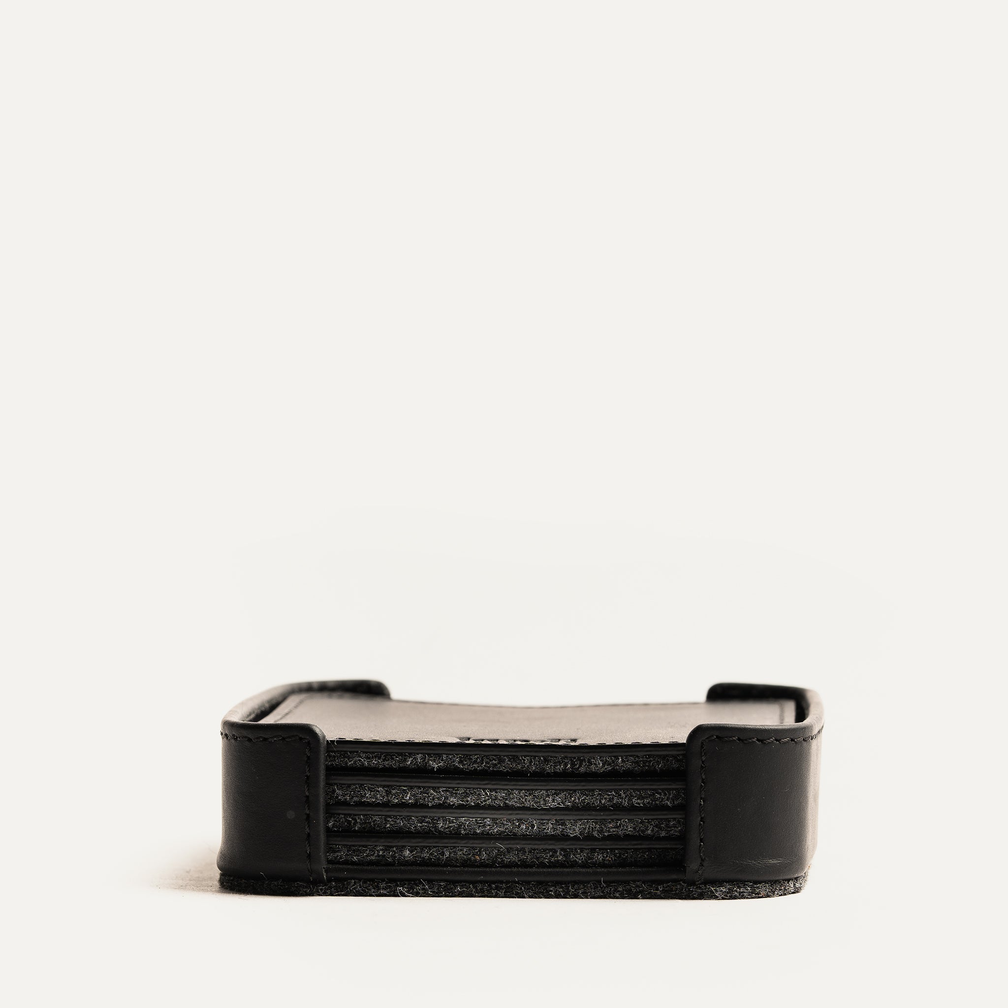 Sous tasse noir en cuir, empilé dans un support vu de face, soulignant la finition haut de gamme.