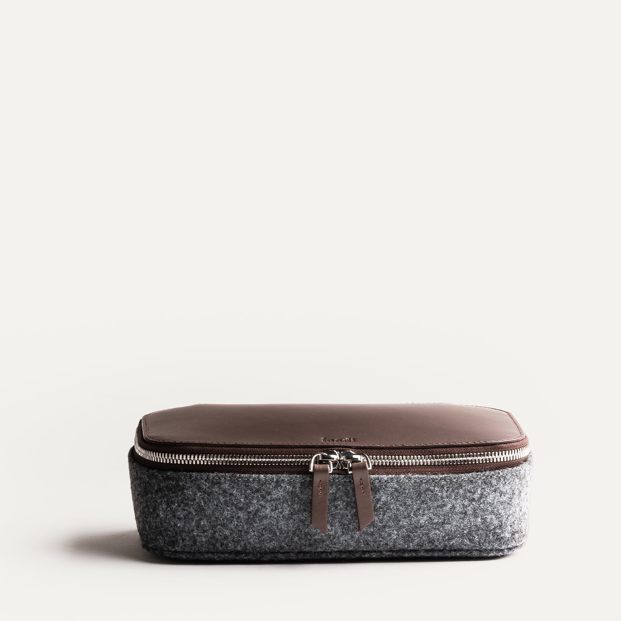 Trousse de toilette de luxe en cuir marron et feutre gris, fermée, avec détails de couture soignés.