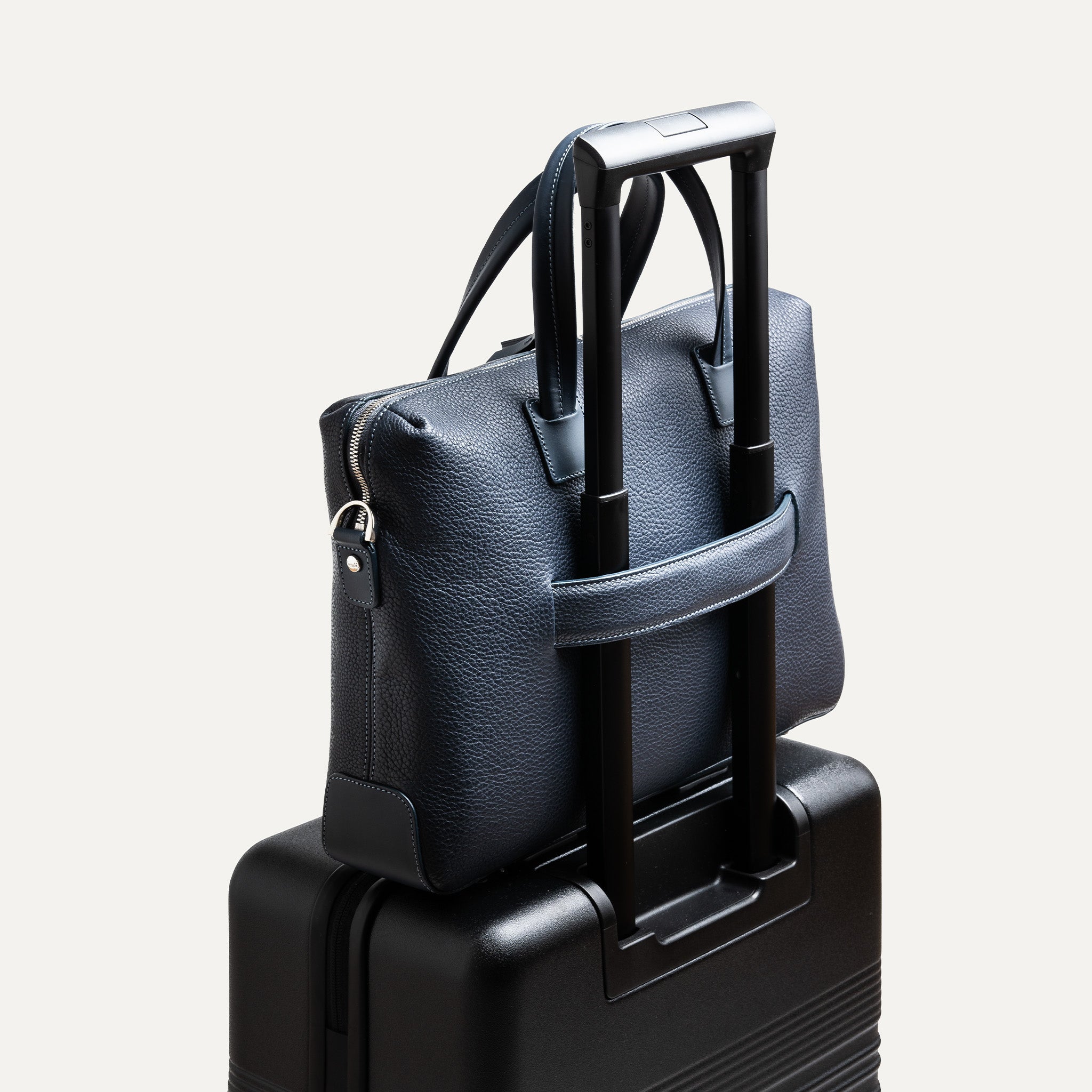 Sac à main homme posé sur une valise avec passant arrière intégré pour faciliter les déplacements.