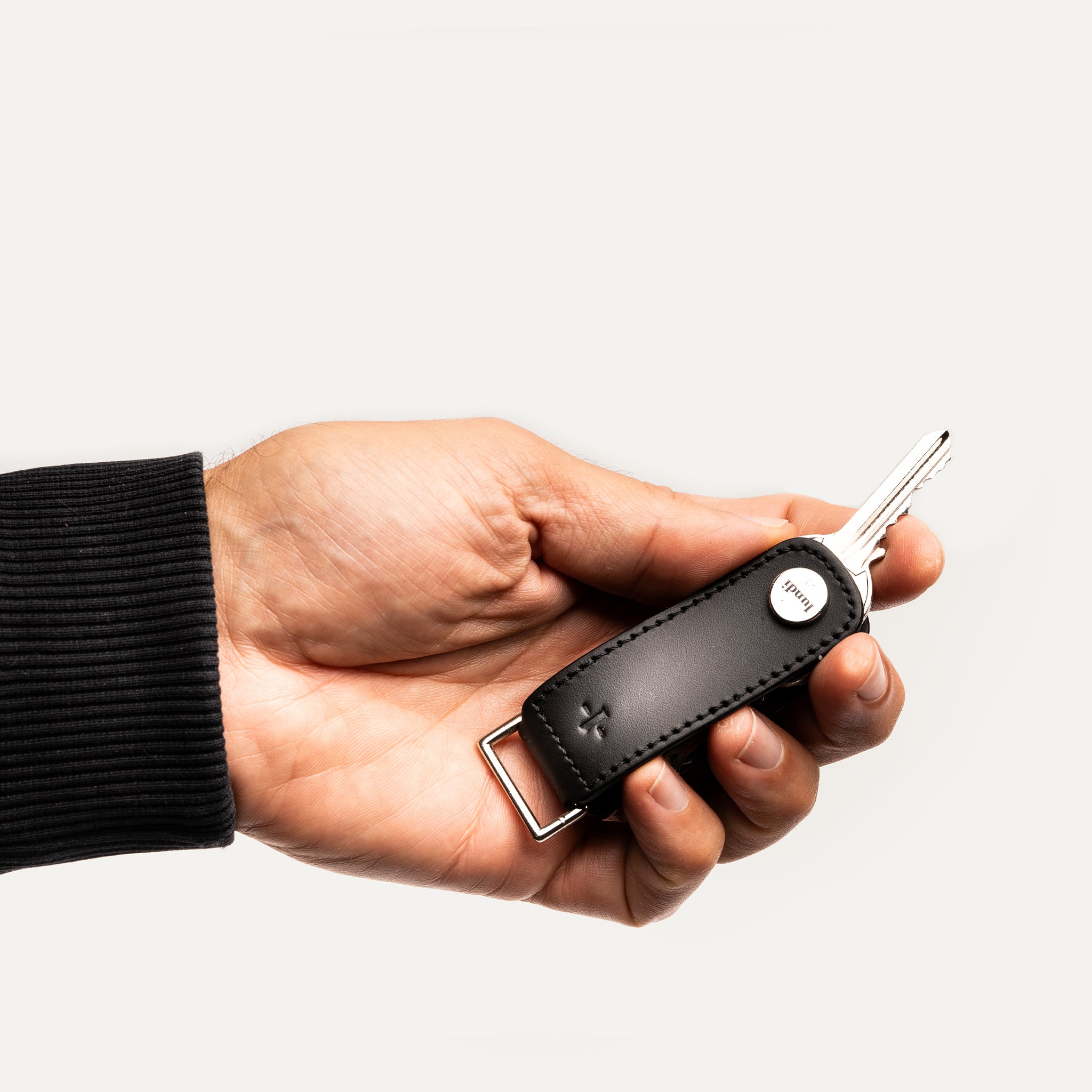 Porte clé pour homme tenu en main, avec clés métalliques rangées dans un étui en cuir noir.
