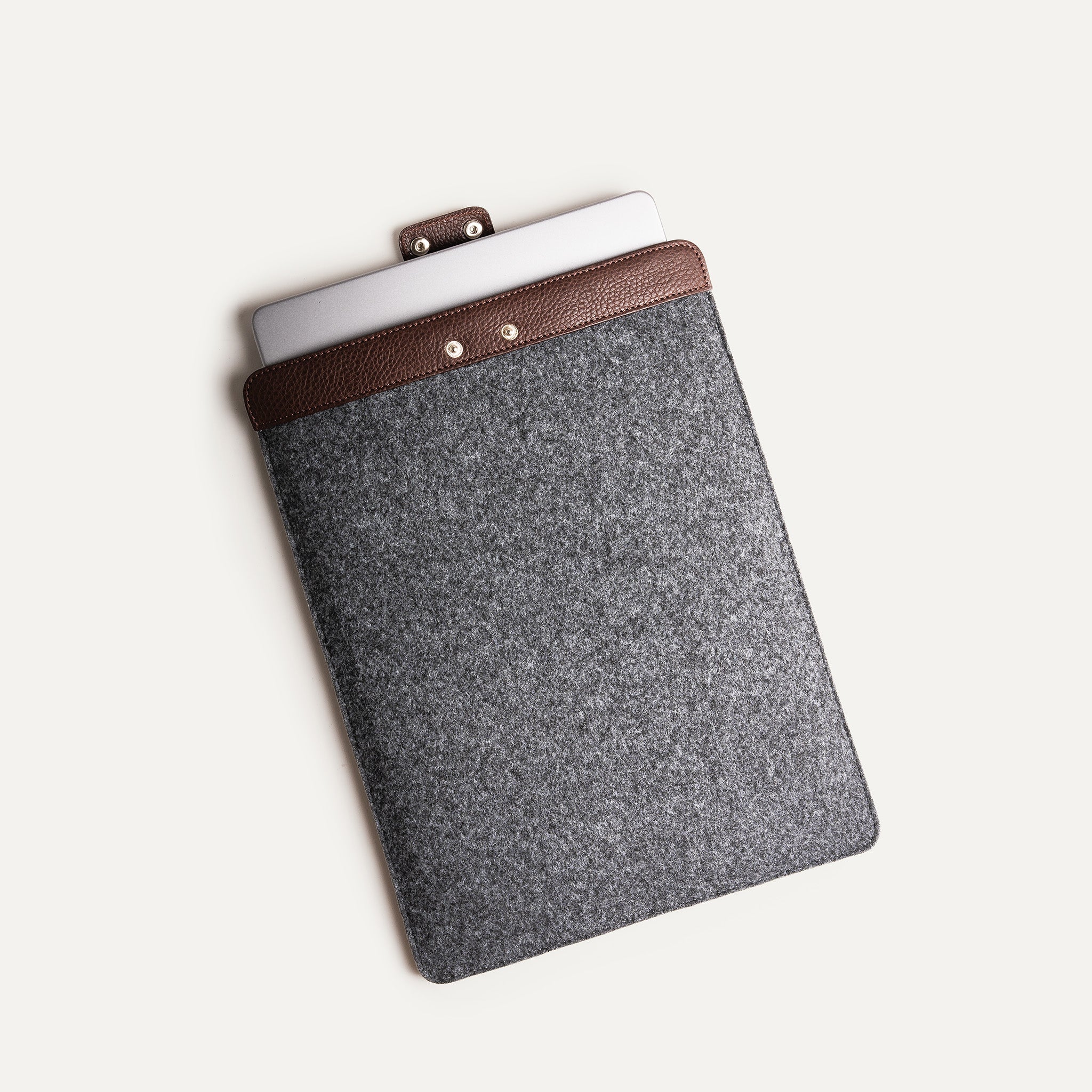 Housse ordinateur avec MacBook inséré, finition cuir marron et fermeture bouton pression.