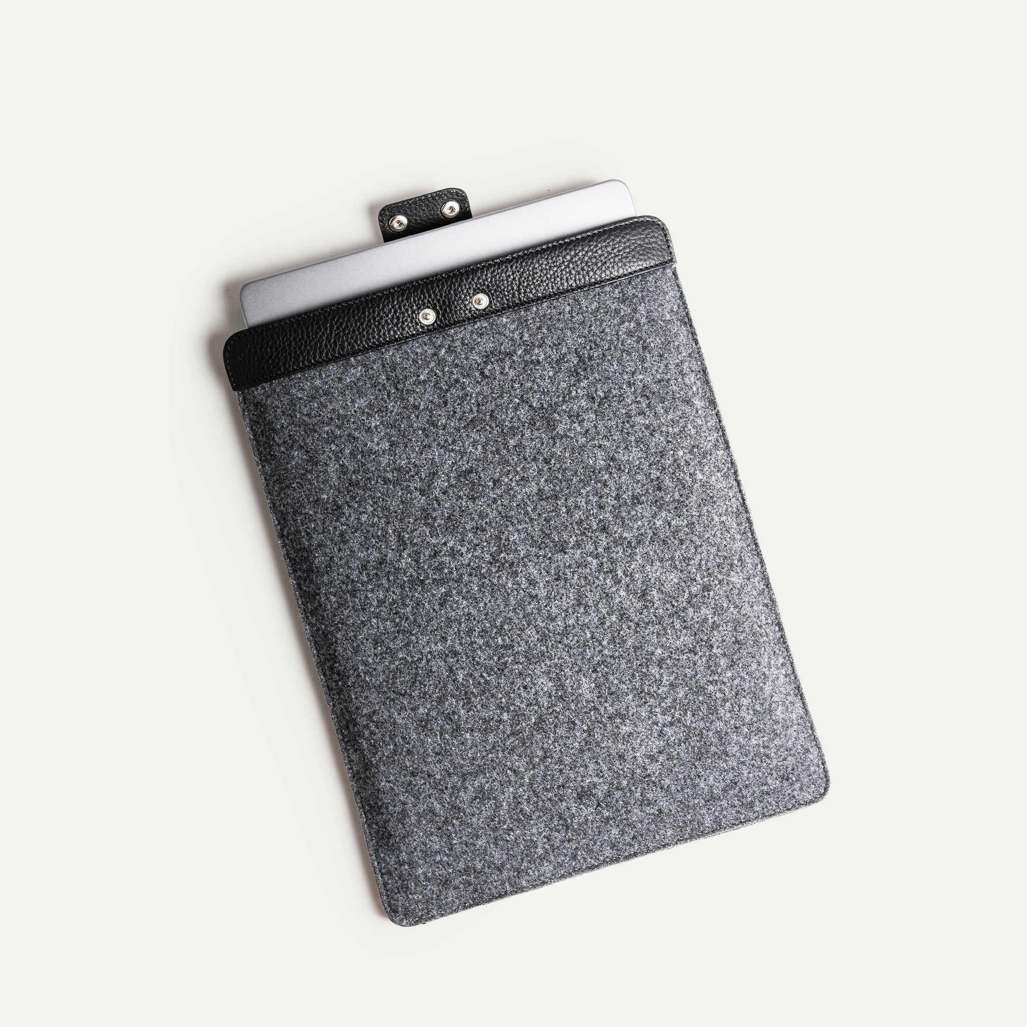Leather laptop sleeve with MacBook partially inserted, secure button closure.