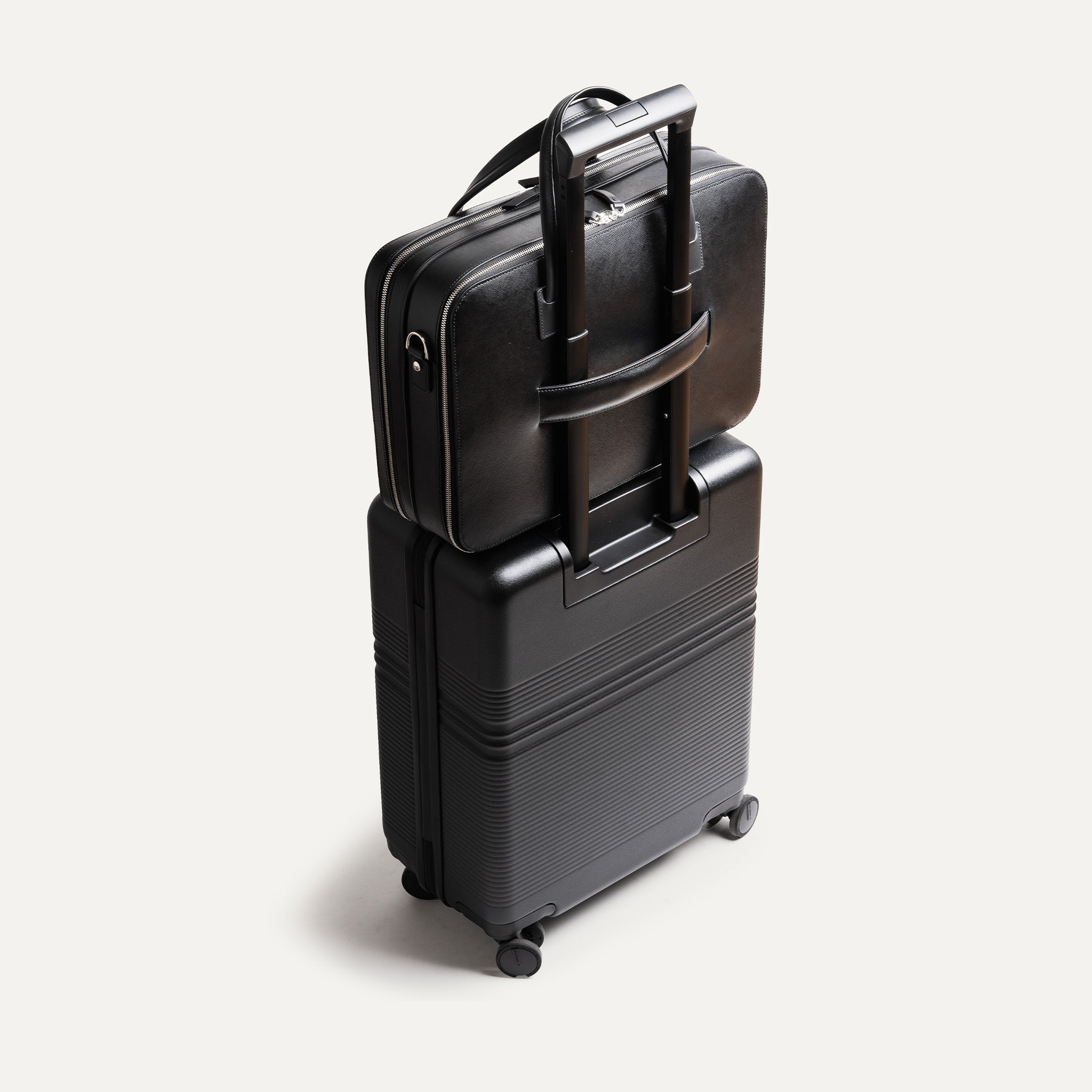 Porte document en cuir accroché à une valise grâce à sa sangle rectractable.