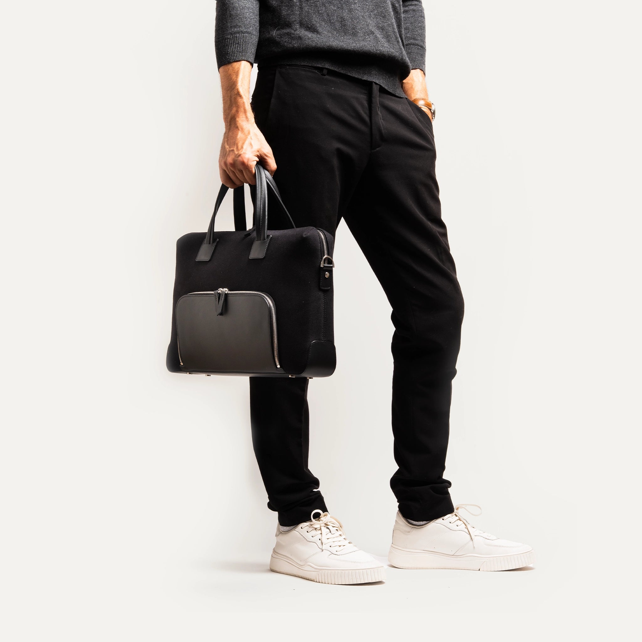 Porte-documents en toile et cuir élégant et compact, de couleur noire, porté par un mannequin.