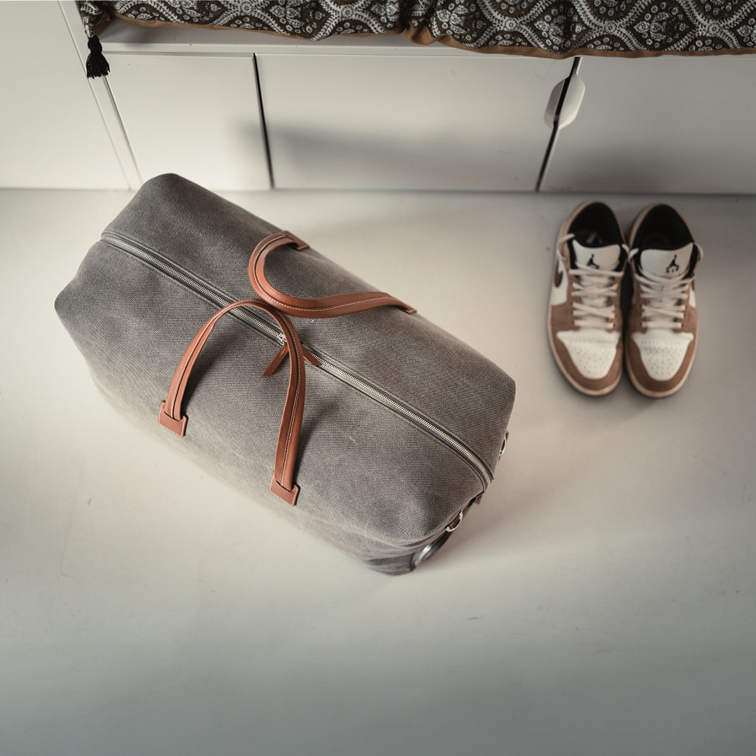 Men’s leather travel bag angled to reveal the side shoe compartment unzipped, displaying white sneakers tucked inside.