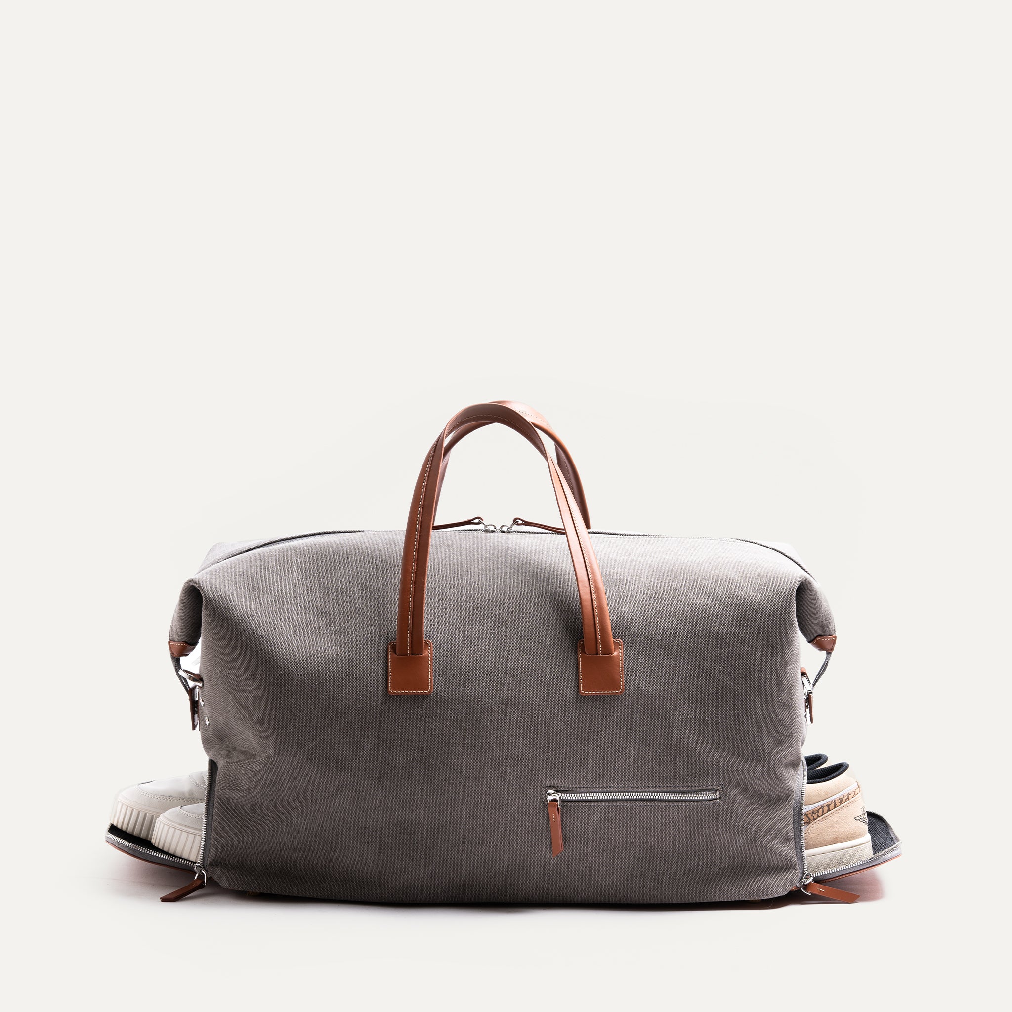 Men’s leather travel bag featuring a detachable shoulder strap and side zip pocket for shoes, suspended.
