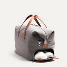 Men’s leather travel bag angled to reveal the side shoe compartment unzipped, displaying white sneakers tucked inside.