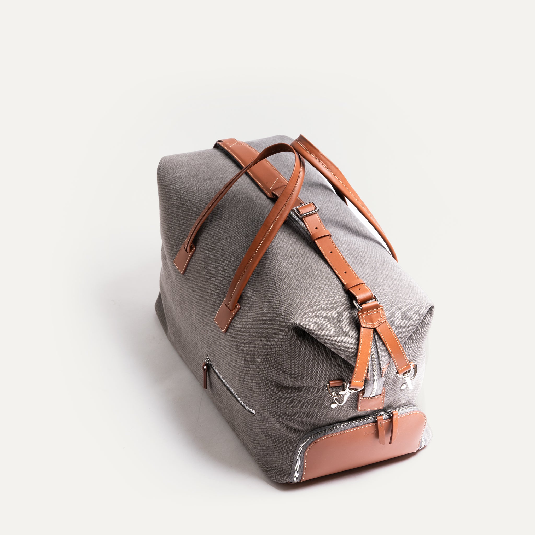 Men’s leather travel bag held by its top handles, highlighting the polished hardware and adjustable shoulder strap.