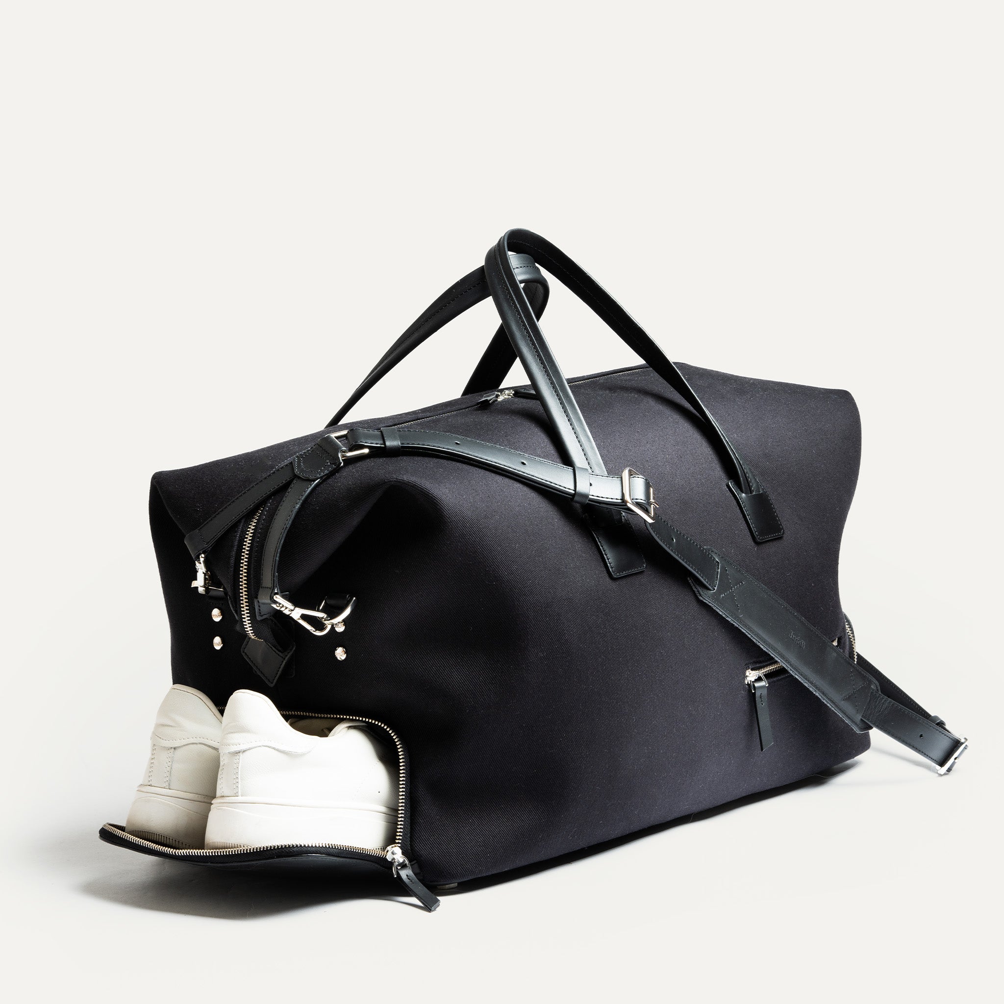 Sac weekender noir avec poche latérale ouverte montrant des baskets, fonction idéale pour les voyages courts ou le sport.