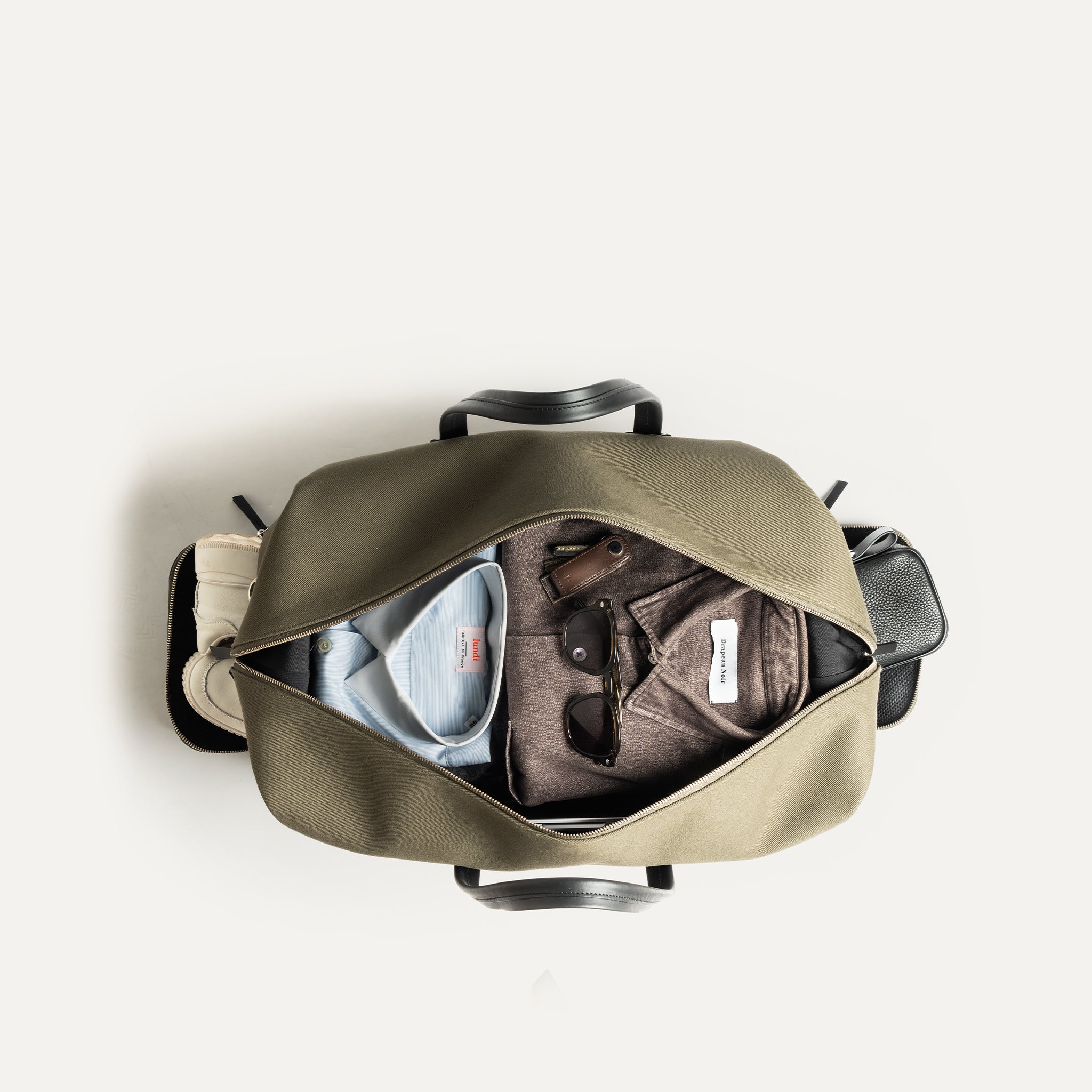 Vue intérieure d’un sac de voyage cabine kaki avec vêtements et accessoires soigneusement rangés.