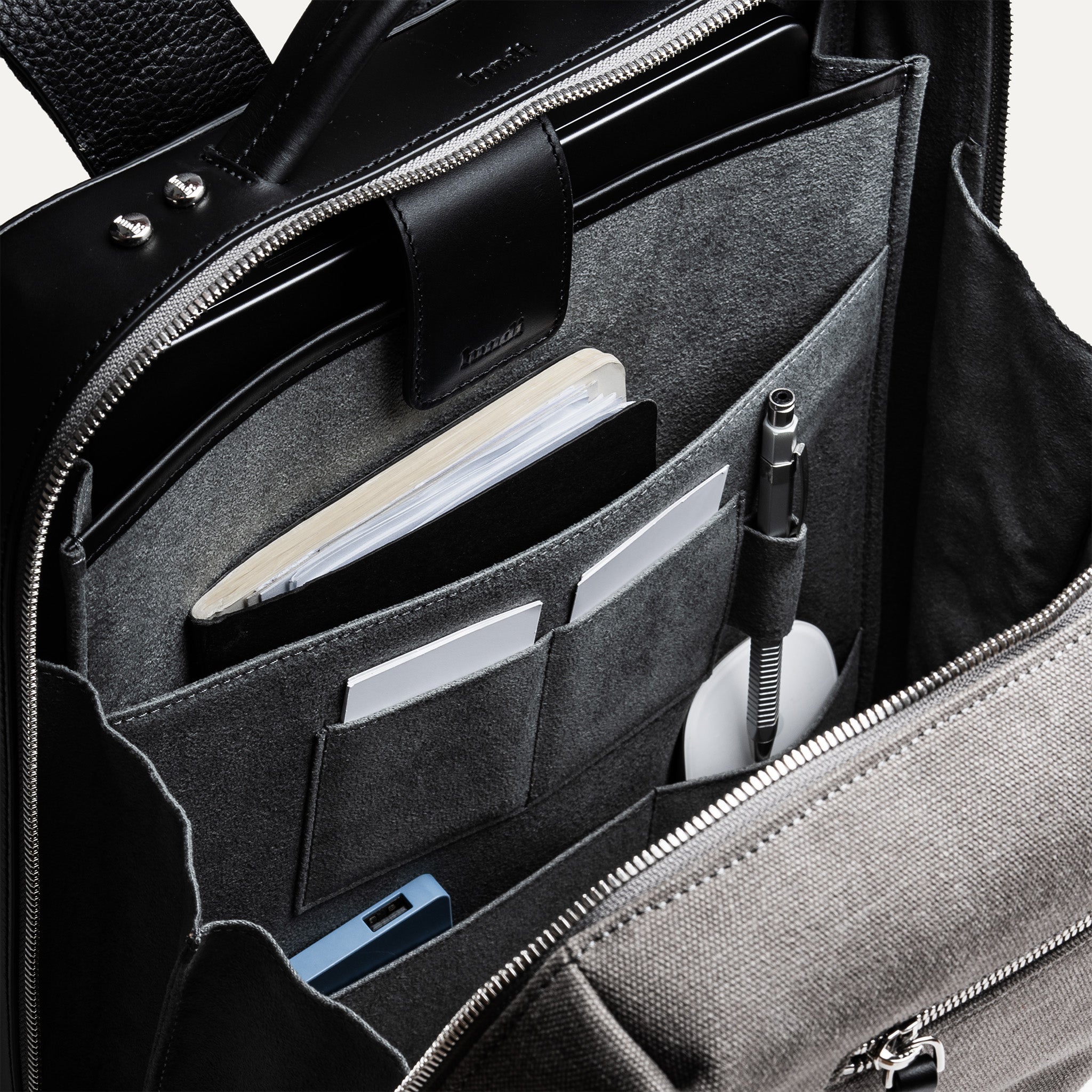 sac à dos homme en cuir et toile grise avec poches tech, stylos, carnet et rangement ordinateur.