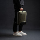 Sac à dos en cuir homme porté à la main avec élégance, pratique pour le travail et l’avion.