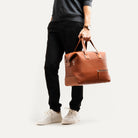 Sac weekender cuir marron porté à la main, élégant et fonctionnel pour déplacements courts et professionnels.