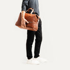 Sac de voyage pour homme en cuir marron porté à la main, adapté au style professionnel ou décontracté.
