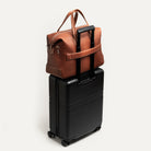 Sac de voyage cabine en cuir marron fixé sur valise trolley, parfait pour voyage d'affaires court.