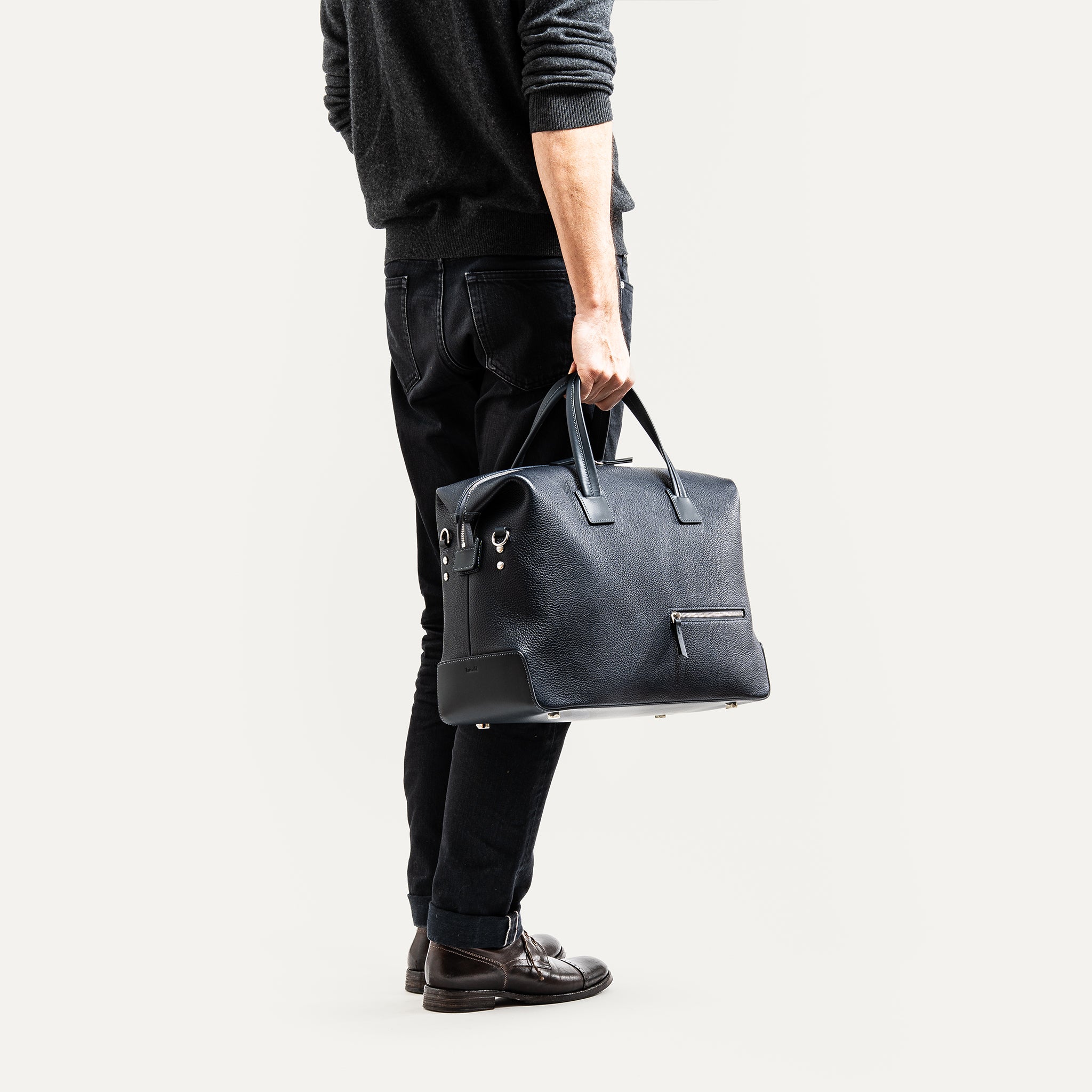 Sac de voyage homme en cuir marine portée à la main avec une allure élégante.