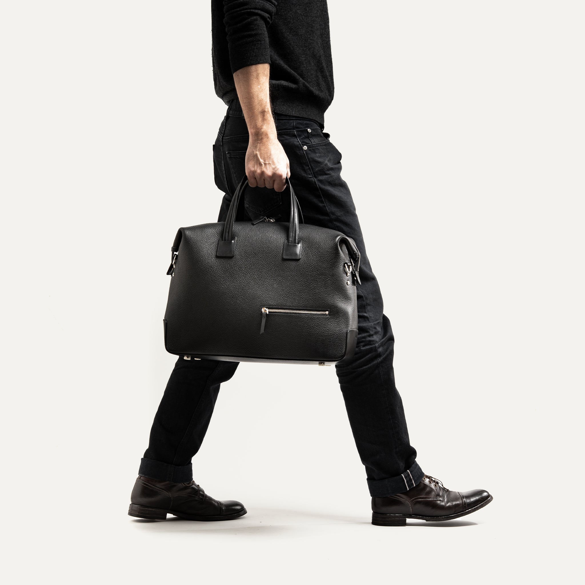 Sac weekender homme cuir noir, style élégant et moderne, porté à la main idéal court séjour professionnel.