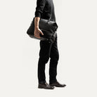 Sac de voyage pour homme en cuir noir porté en bandoulière, parfait pour voyages d'affaires ou loisirs.