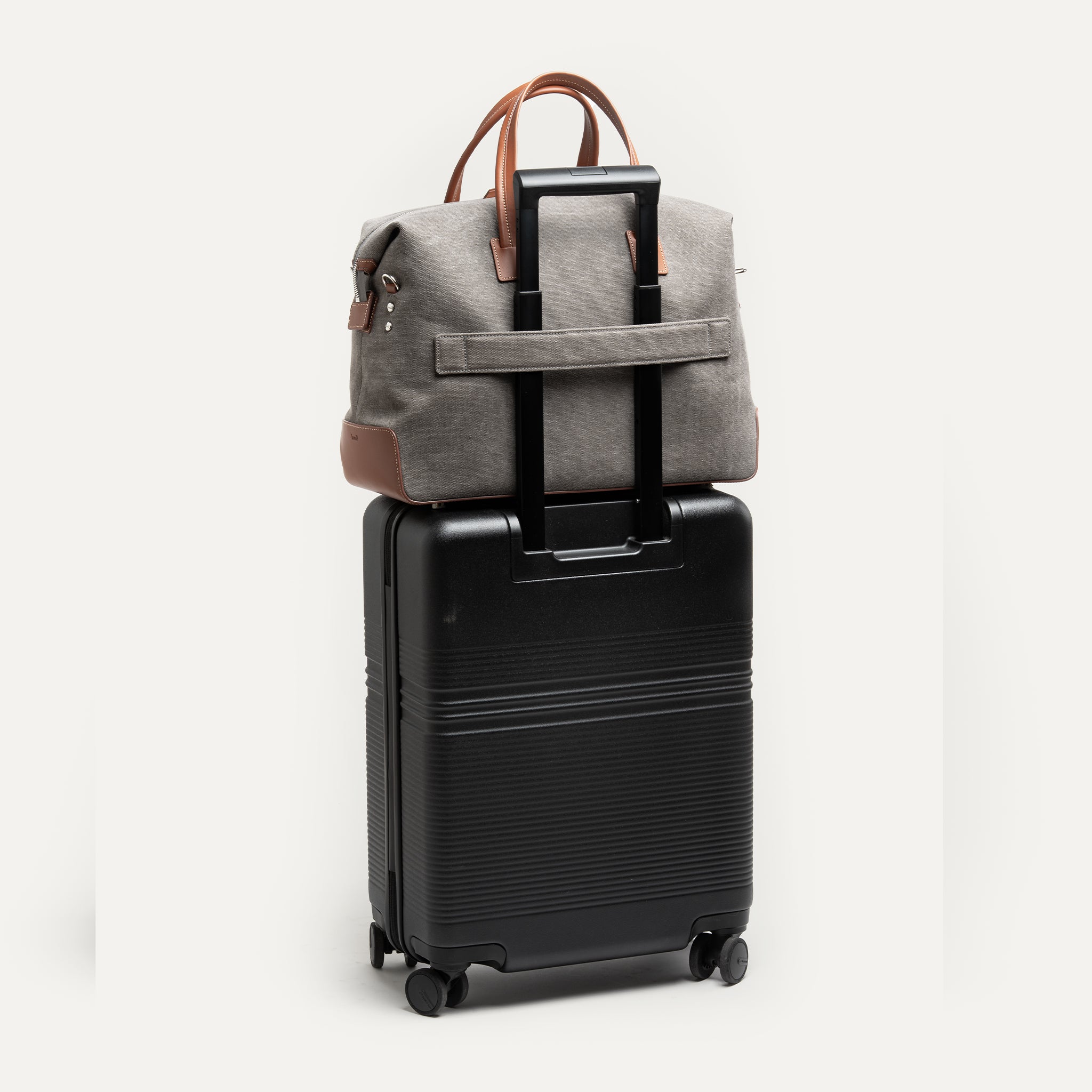 Sac weekender AUGUSTIN en toile grise et cuir cognac avec un option passant trolley pour s'adapter à une valise.