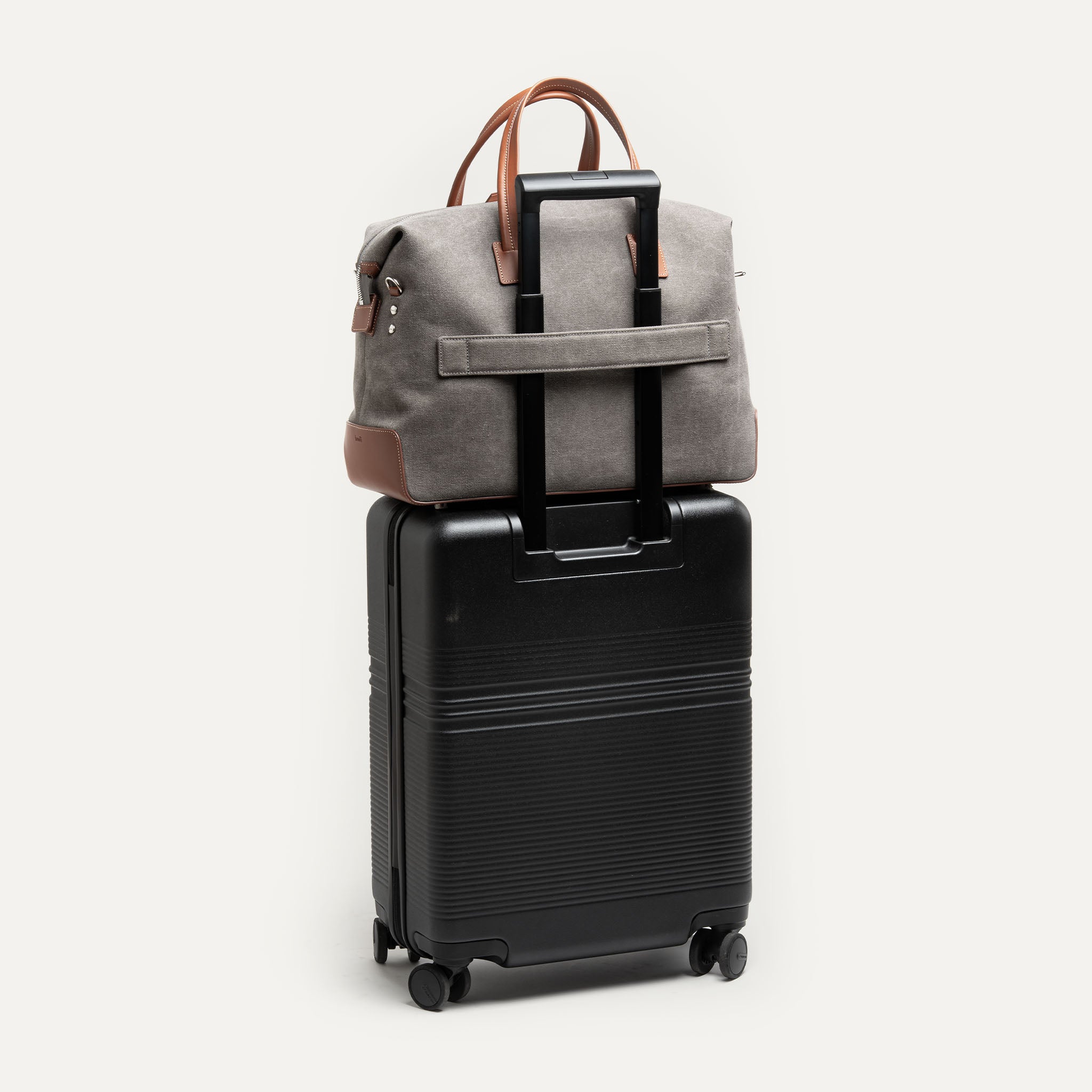 Sac weekender AUGUSTIN en toile grise et cuir cognac avec un option passant trolley pour s'adapter à une valise.