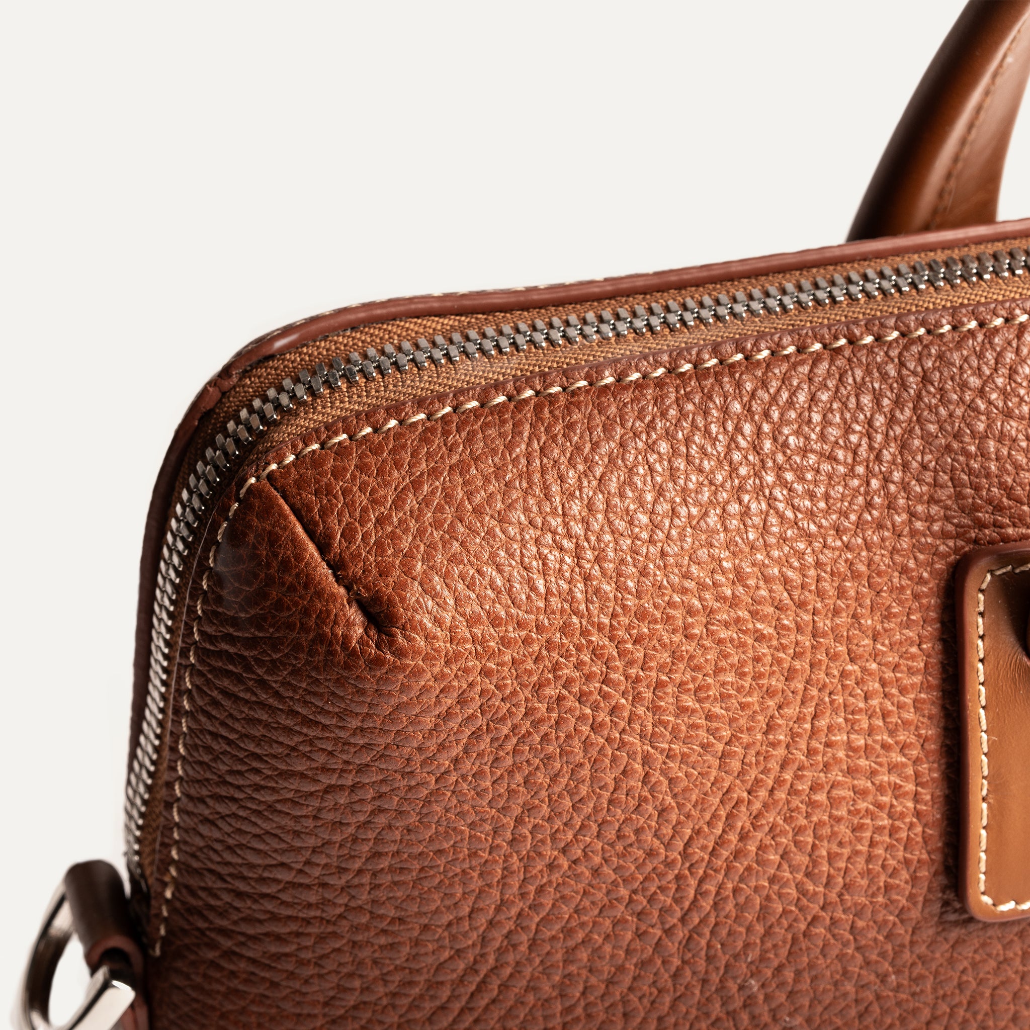 Briefcase haut de gamme en cuir grainé camel, avec finitions soignées et zip robuste.