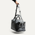 Sac de voyage en cuir noir conçu pour être compact et spacieux, dispose d'un espace de rangement pour vos vêtements et une poche pour ordinateur portable jusqu'à 15 pouces.