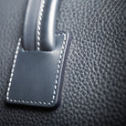 Sac de voyage lundi composé de cuir grainé sur la plupart du sac et de cuir lisse sur les anses et les poches extérieures.