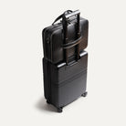 Porte document en cuir accroché à une valise grâce à sa sangle rectractable.